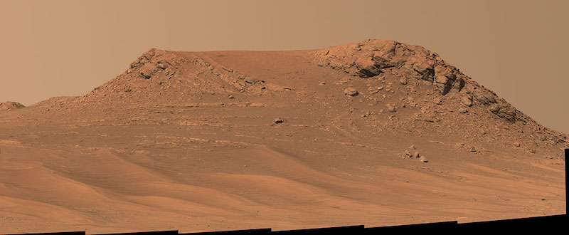 Reddish, rocky mesa-like hill with dusty, reddish sky above.