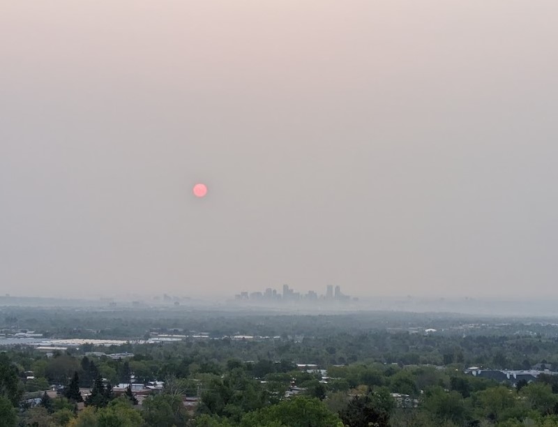 View looking at a skyline with smoke below some of the towers and in the sky, creating a red sun.