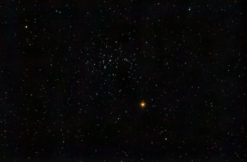 Cielo estrellado con un cúmulo de docenas de estrellas relativamente juntas con un Marte rojo brillante cerca.