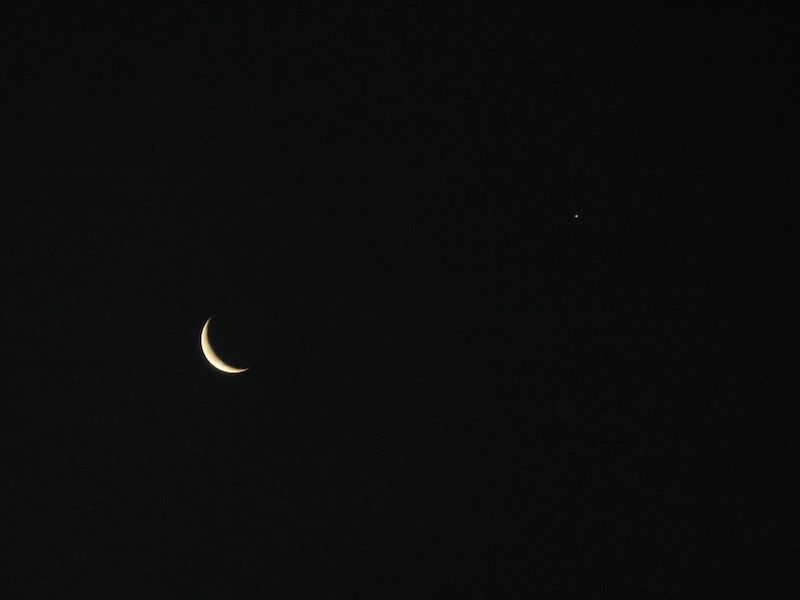 Crescent moon against dark sky with a small dot that is Jupiter.