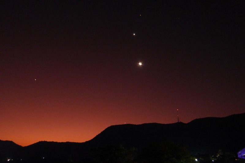 Orange sky with a mountain at the bottom and 3 bright aligned dots at the top.