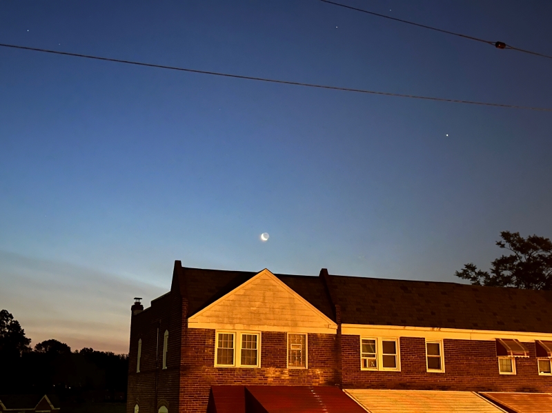 Waning crescent moon rising above a house in a dawn sky, with Jupiter as a small bright spot nearby.