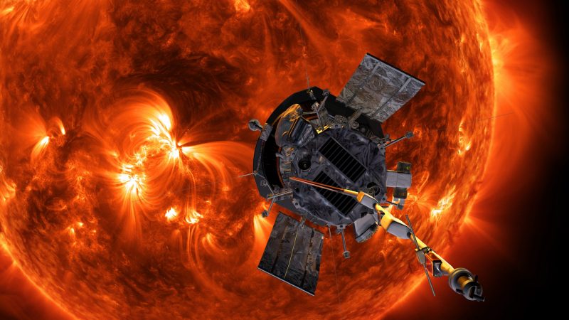 Spacecraft in front of the sun's face which has dark and bright spots and loops.