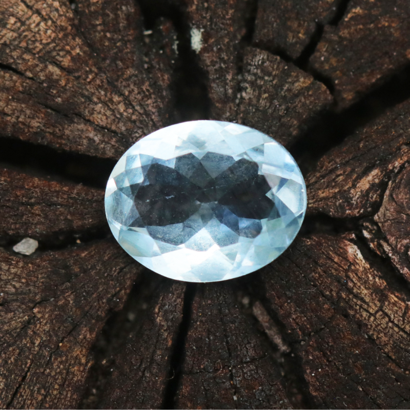 Round bluish brilliant gem with a piece of wood as a background.