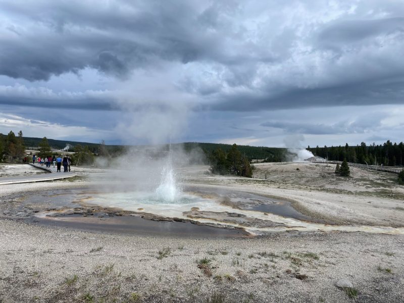 Water erupting from bare gray ground, under a cloudy sky.