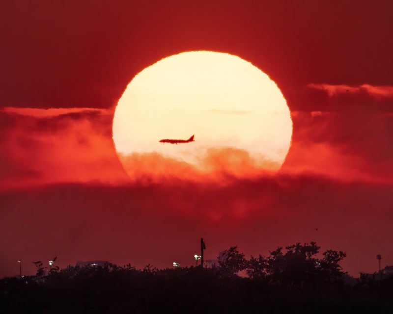 Sunset through orangish clouds and airplane in front of the sun.