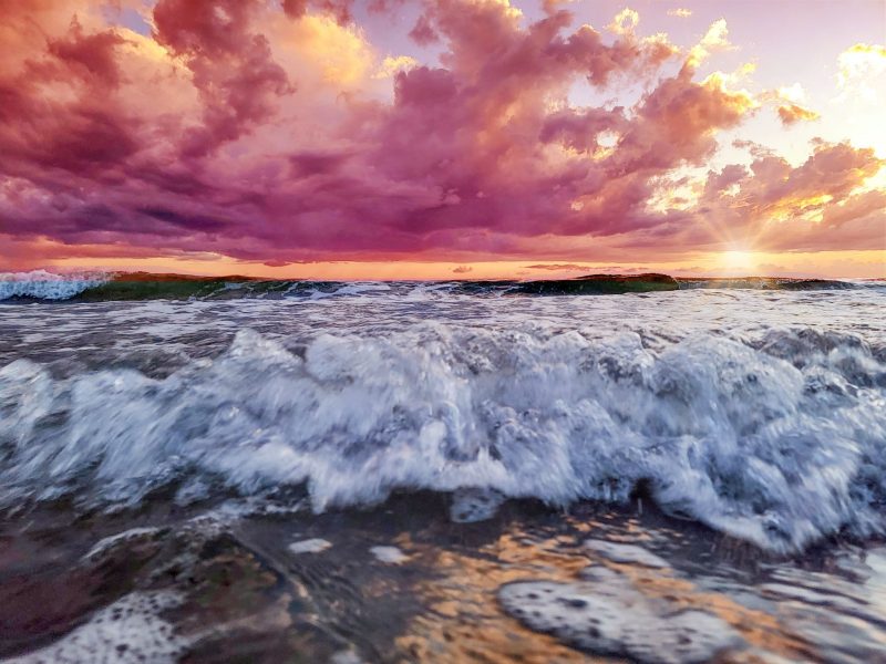 Tides: Turbulent incoming waves under a sky full of pink and orange clouds.