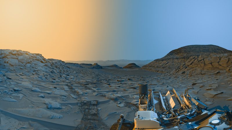 A landscape of Mars with robot in front and sky half orange and half blue.