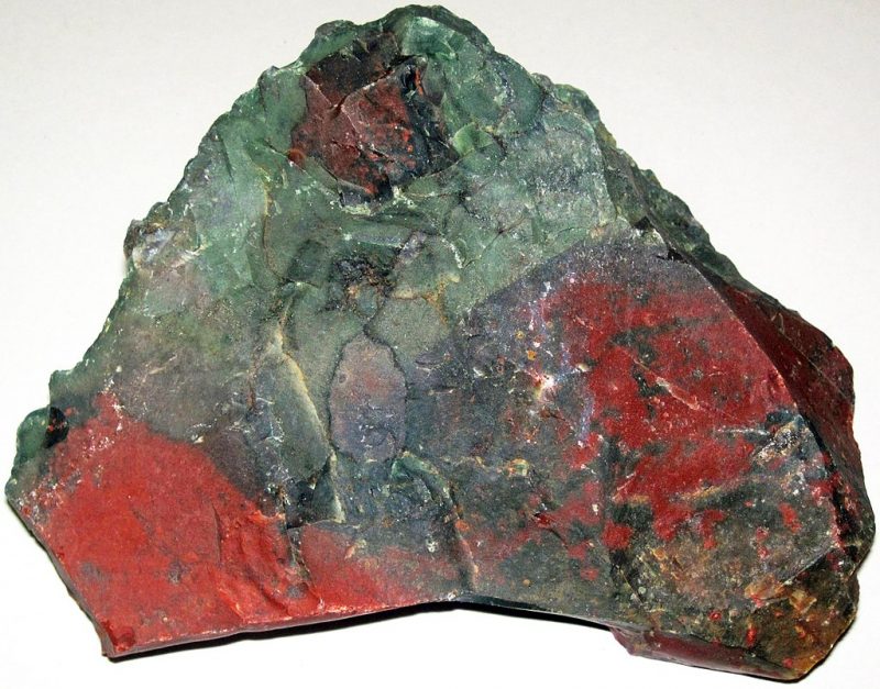 Triangular grey and red rock with some tones of green in the middle and orange at bottom right.