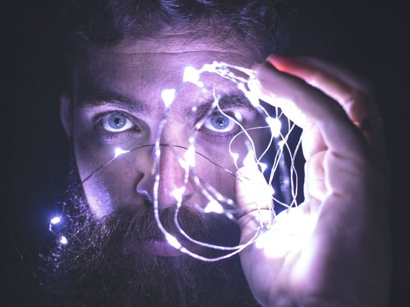 Uploading our minds: Man holding a string with beads of light, looking at camera.