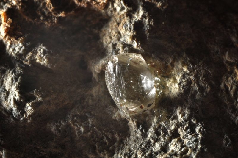 Transparent round gem embedded in a wall made of rock.