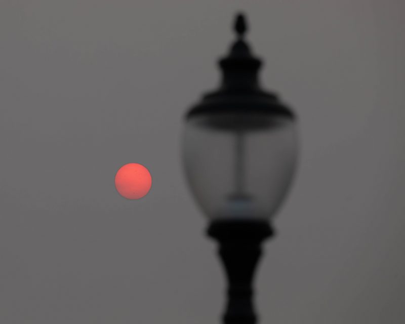 Reddish sun in deep gray sky behind a lamppost.