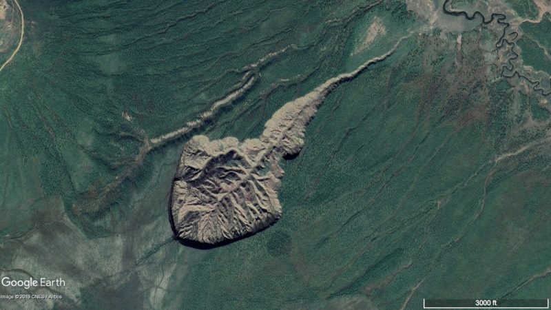 Tadpole-shaped brown scar filled with gullies, in green landscape.