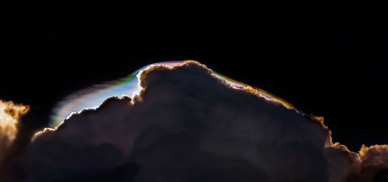 Dark cloud with cap of rainbow colors on dark sky.