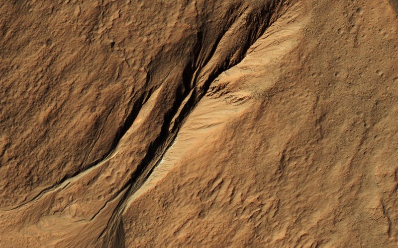 Orbital view of long valley-like feature in reddish terrain.