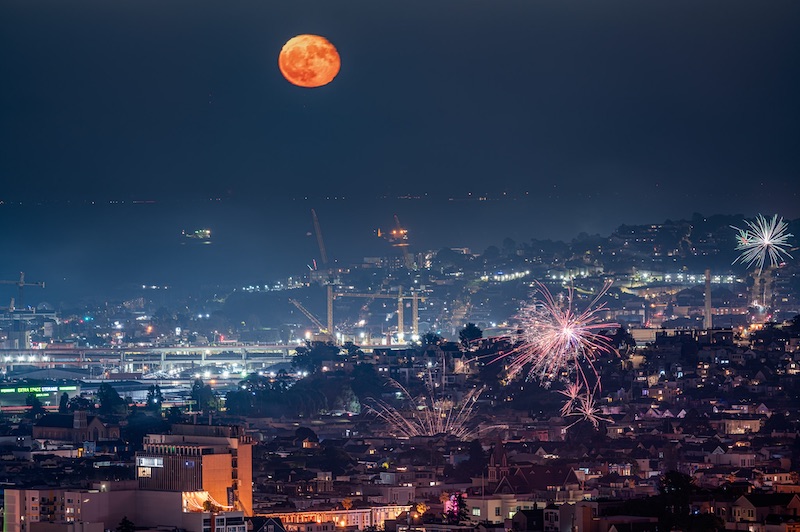 Waning gibbous moon over night cityscape with fireworks.