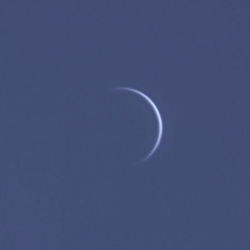 A very thin crescent Venus, like a featureless, slightly fuzzy crescent moon.