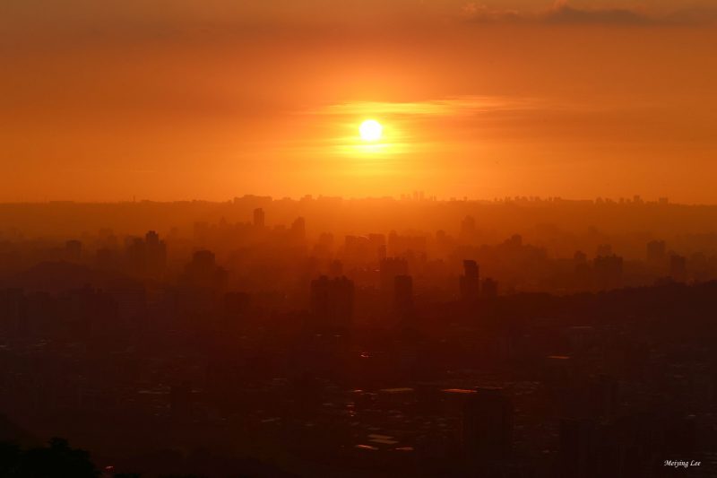 Record temps: Sun sets in orange sky over rows of city buildings from foreground to horizon.