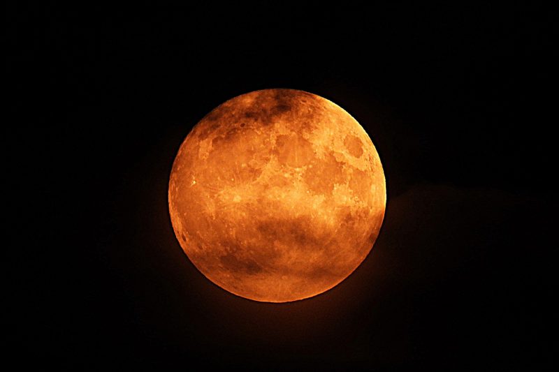 Orange, bright moon less visible at top and bottom because of the clouds.