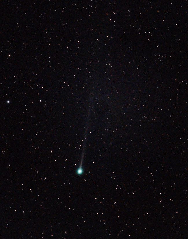 Dark sky with stars and bluish-green bright orb with a long, thin streamer off it.