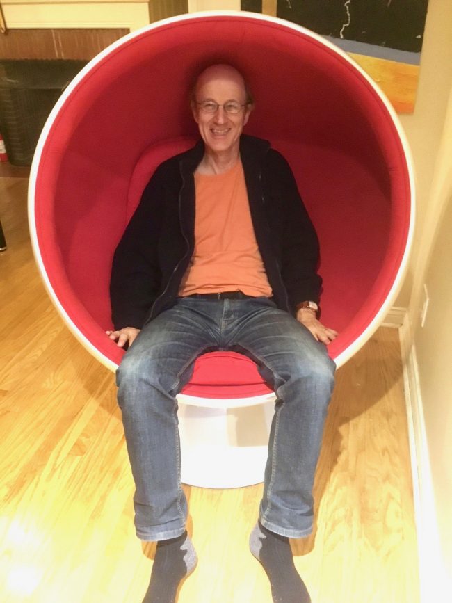 Smiling, casually dressed man sitting in a bright red circular chair.