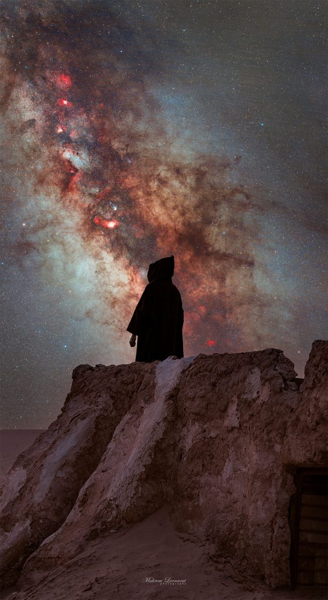 Hooded person standing on hill with Milky Way in background.