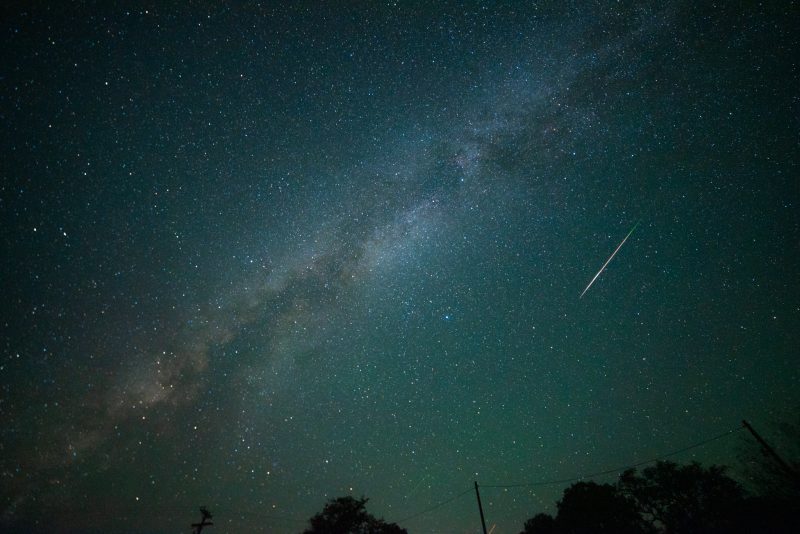 Meteor showers: In greenish sky, fuzzy band of Milky Way, and a single thin bright streak.