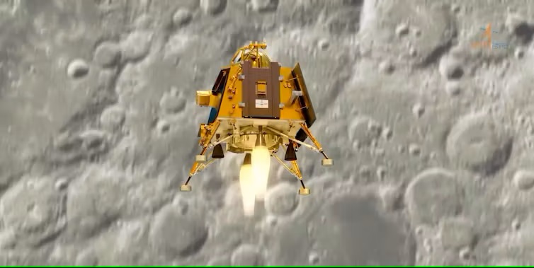 Moon landing for India: Graphic of a golden colored spacecraft with 4 legs and 2 rockets over the moon's gray, cratered surface.