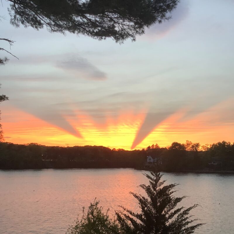 Sunset view with dark rays cut into the orange glow and over a lake.