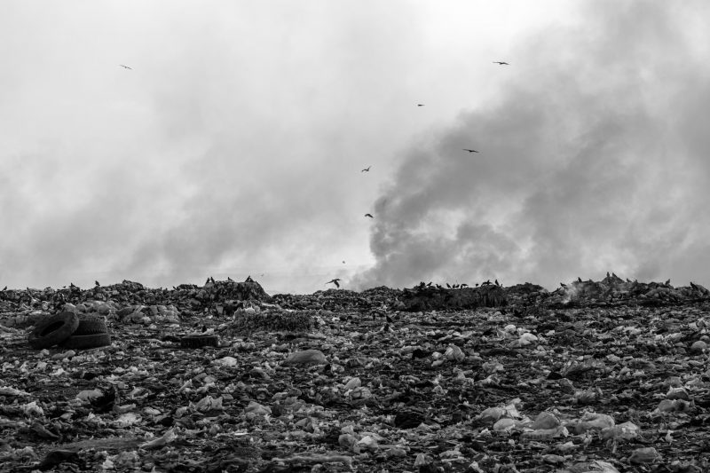 Rising methane: Black-and-white image of huge field of trash with smoke in background and a few black birds in the sky.