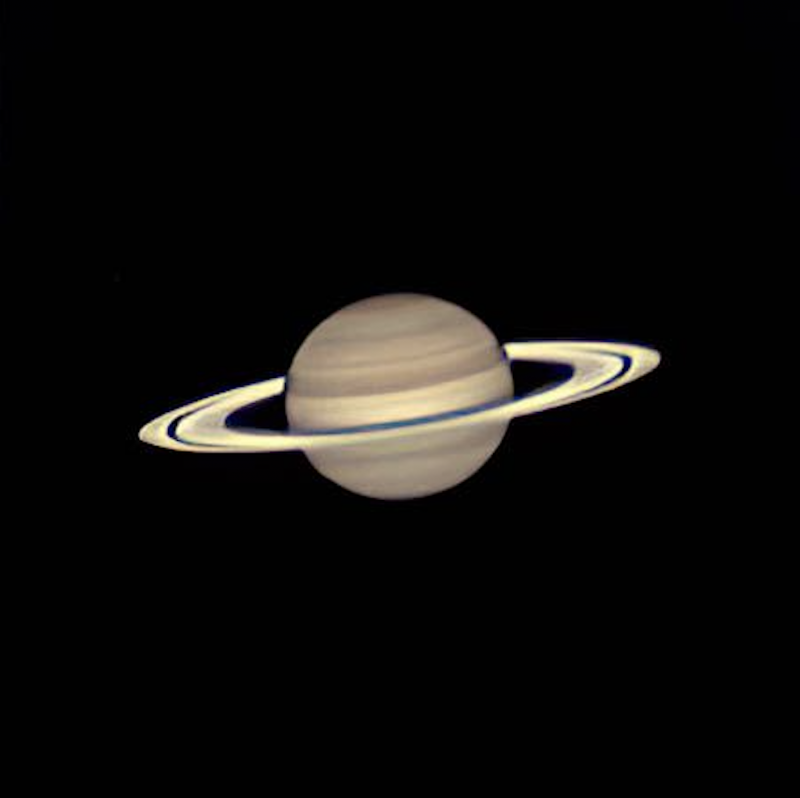 Saturn: Golden ball, surrounded by oblique rings, on black background.