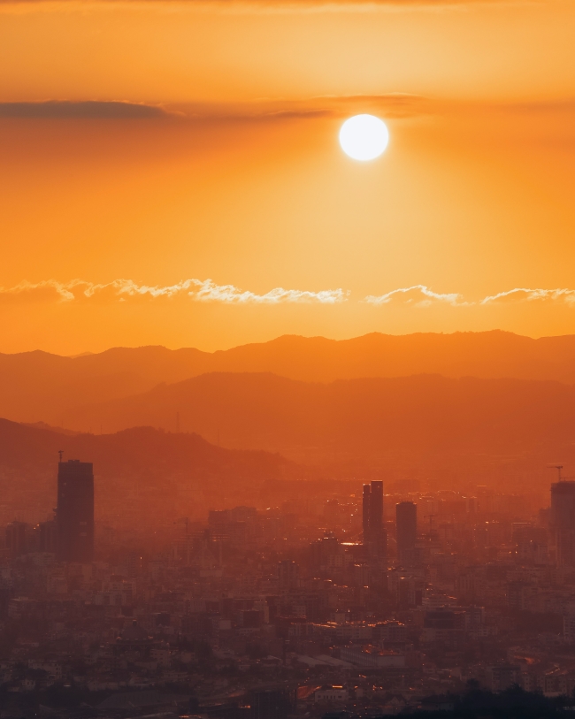 bright sun setting over a city in the foreground and large mountainous hills in the background