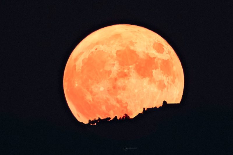 Large orangish moon rising over a hillside.