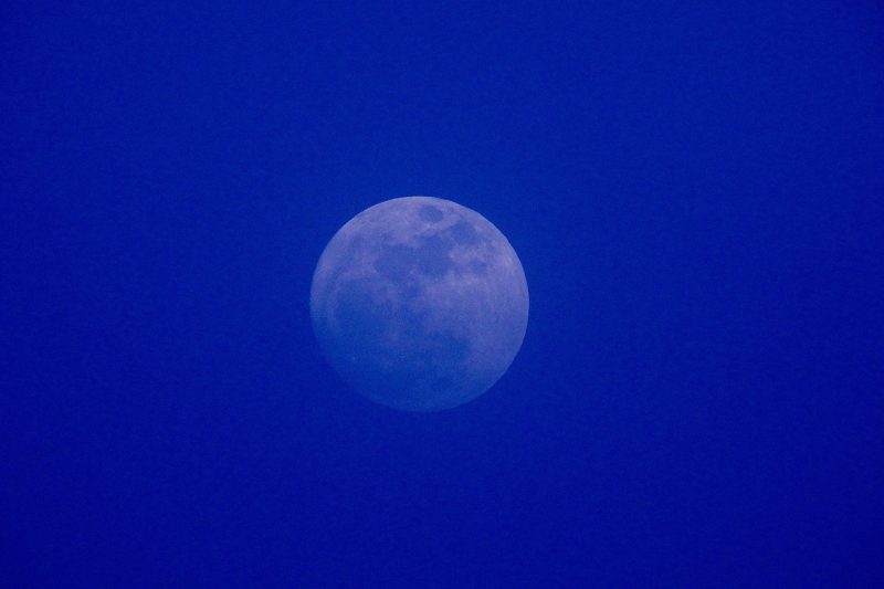 Full moon in a haze of blue, darker at bottom.