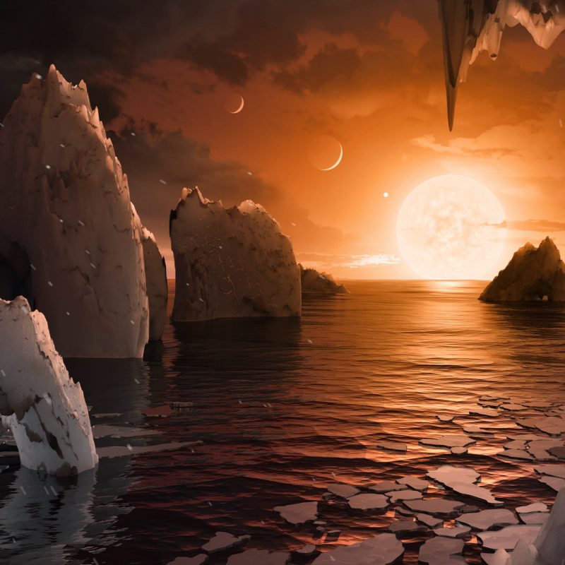 Iceberg-filled ocean under orange sky with several crescent planets and large sun.
