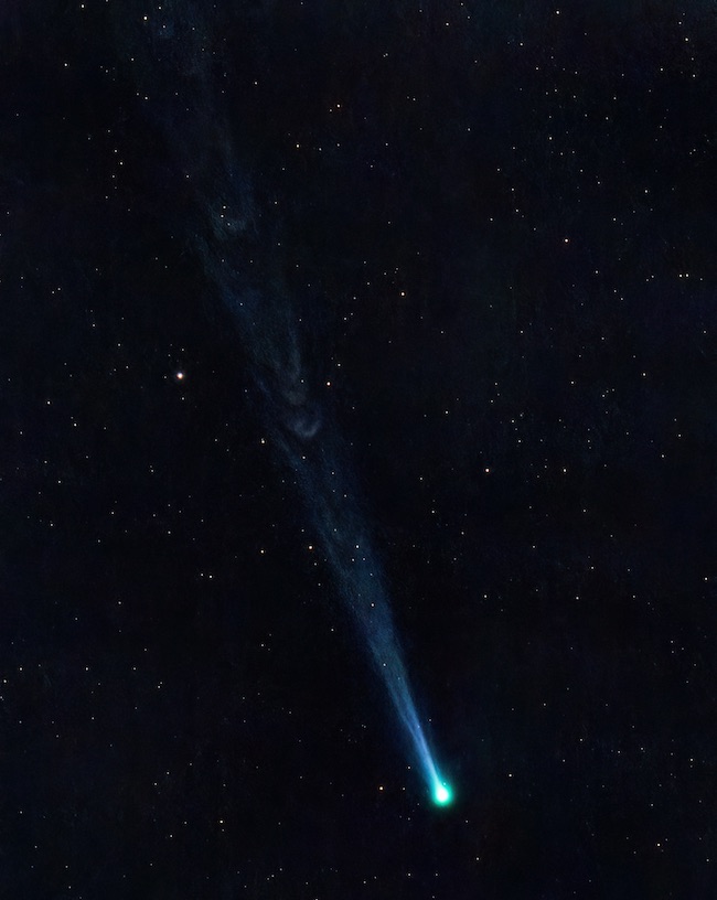 Dark, starry sky with greenish-blue comet head and tails streaming away from it.