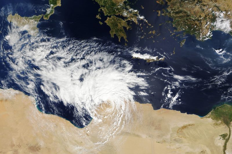 Extreme rainfall and flooding: Satellite image shows spiraling white clouds in a storm over part of the sea and some tan ground.