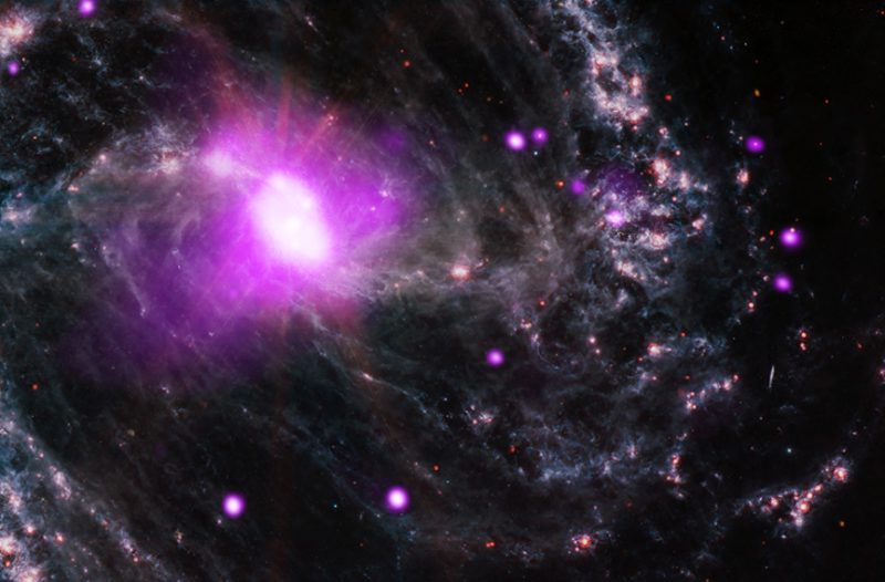 Smallish glowing white oval surrounded by magenta halo and stringy, wispy spiral arms.