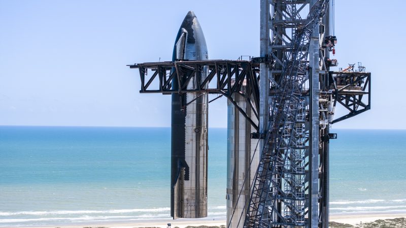 SpaceX Starship: Blue sea and blue sky at the background, with silver bullet-shaped rocketship girders in the foreground.