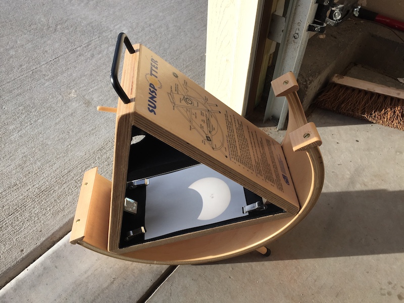 Wooden device with a semicircle base, a triangular insert projecting a picture of an eclipsed sun on white paper.