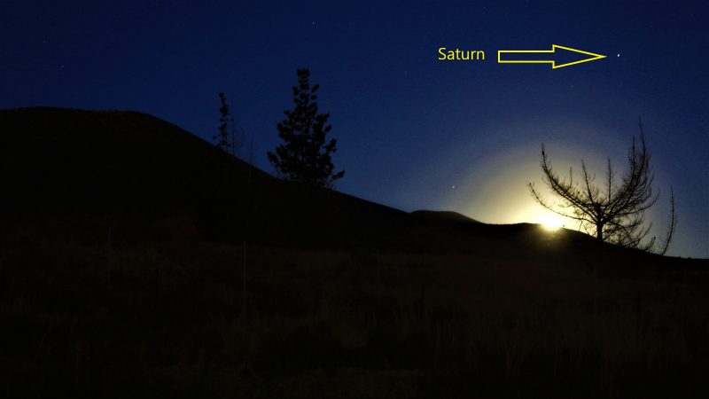 A glowing moonrise above the rim of a mountain, with labeled Saturn nearby.