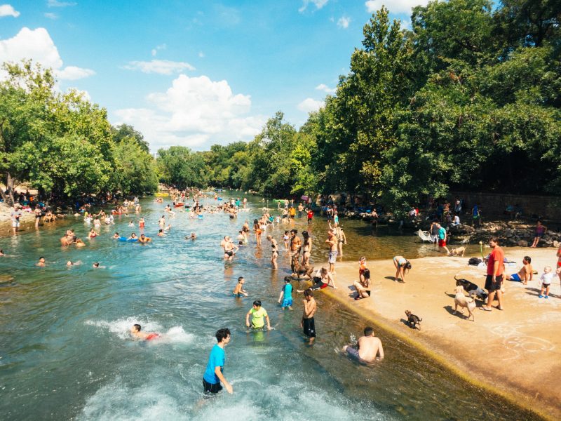 Earth: Many people wading in a wide creek between trees.