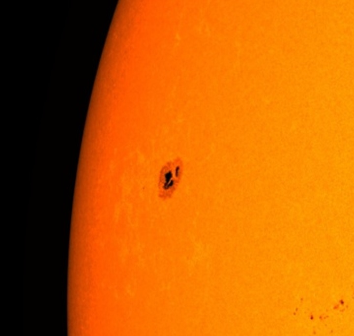 Closeup of one edge of the orange sun showing a dark collection of spots with a lighter ring around them.