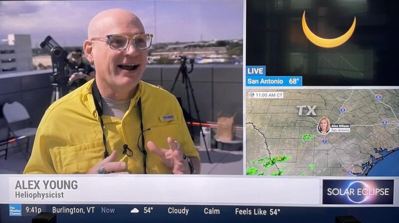 A smiling man in a yellow shirt talking on TV screen with insets of an eclipsed sun and a weather radar.