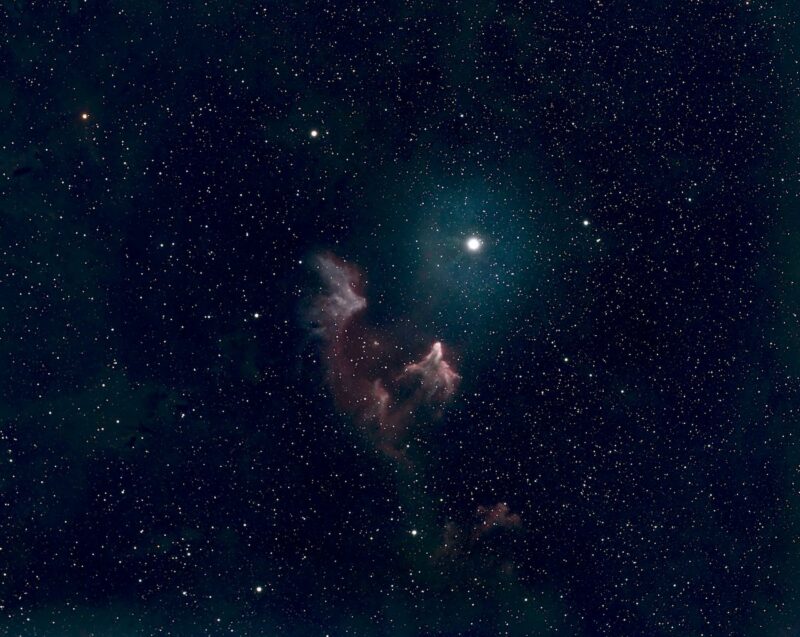 Reddish C-shaped nebula near a bright star, in faint star field.