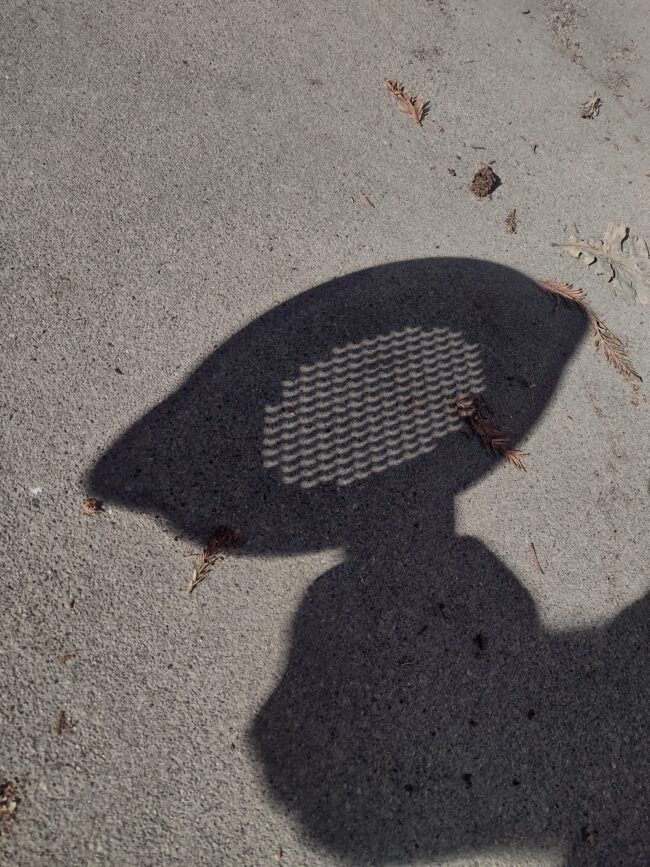 The shadow of a hand holding a kitchen strainer, with an array of tiny bright crescents within the shadow.