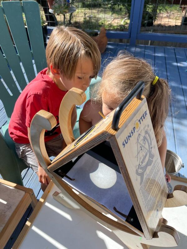 A young boy and girl look down at a device showing a projection of a partial eclipse and some sunspots.