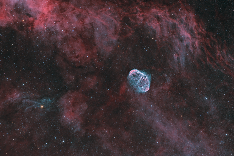 Bluish cocoon of gas over red nebulous swirls and a background of faint stars.