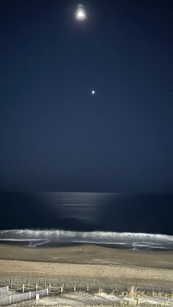 An early morning beach scene with waves across the bottom with the Moon and Venus on the top.