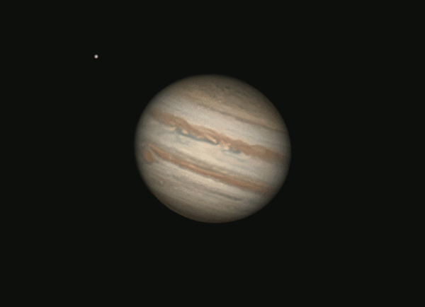 Tan, banded Jupiter rotating, with the big oval red spot crossing it, and two bright dots for moons nearby.